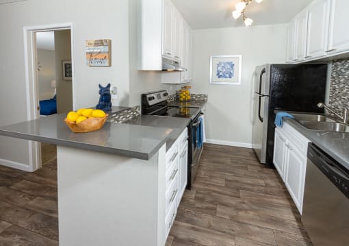 Downey CA Apartments for Rent - Park Regency Club - Kitchen with Multi-Colored Backsplash, Grey Countertops, White Cabinets, and Stainless Steel Appliances.