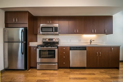 SW Portland, OR Apartments - Corbett Heights - Kitchen with Wood-Style Flooring, Stainless Steel Appliances, Dark Brown Cabinetry, Quartz Countertop, and Silver Hardware