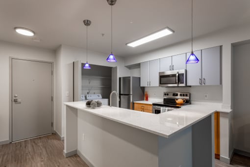 Apartments for Rent in Fremont, WA - Epicenter - Kitchen with Island, Modern Light Fixtures, Wood-Style Flooring, Granite Counters, and Stainless-Steel Appliances