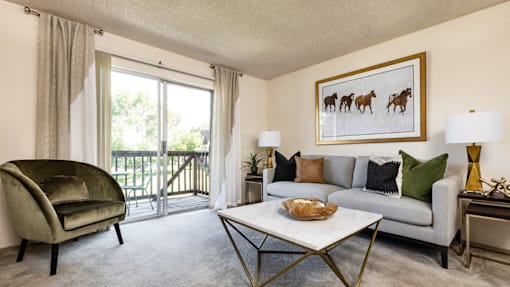 A living room with a grey couch, a green chair, and a painting of horses on the wall.