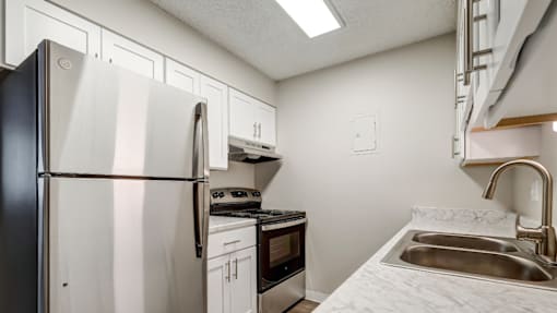 Aurora, CO Apartments – Ivy Crossing – A kitchen with a fridge, white cabinets, and a stove top oven.