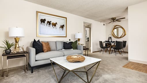 A living room with a grey couch, a coffee table, and a painting of horses.