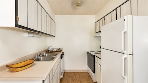 Aurora, CO Apartments – Ivy Crossing – A kitchen with a white refrigerator and a wooden bowl on the counter.