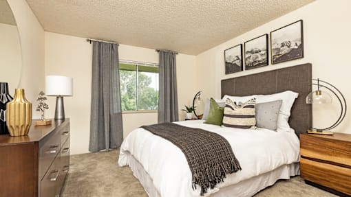 A bedroom with a large bed, a nightstand, and a window with curtains.