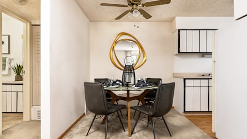 Aurora, CO Apartments – Ivy Crossing – A dining room with a round mirror and a table with chairs.