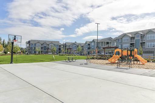 A playground with a basketball hoop and a slide in front of apartment buildings.