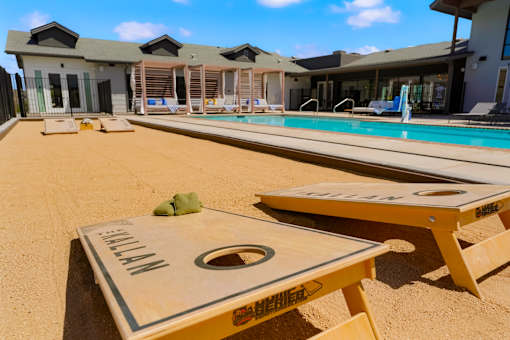 A sand volleyball court is in the foreground of a resort with a pool and lounging area in the background.