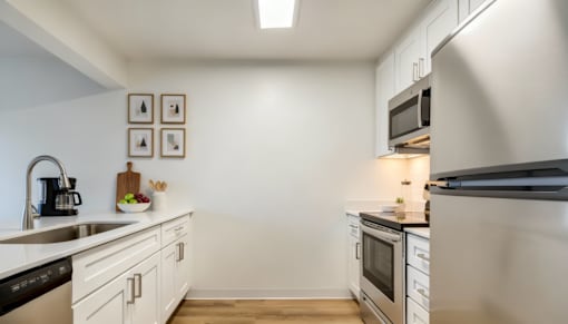 Everett, Washington, Apartments - Woodbrook - Kitchen With Stainless Steel Appliances, Vinyl Plank Flooring, Quartz Countertops, White Cabinets, And A Breakfast Bar.