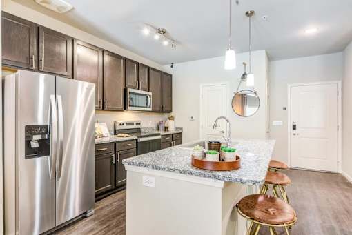 A kitchen with a refrigerator, microwave, oven, and sink.