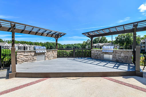 A wooden pergola with a stone wall and a building in the background.