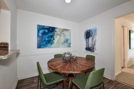 A dining room with a round wooden table and four green chairs.