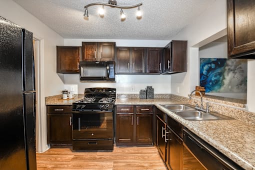 A kitchen with a black refrigerator and brown cabinets.