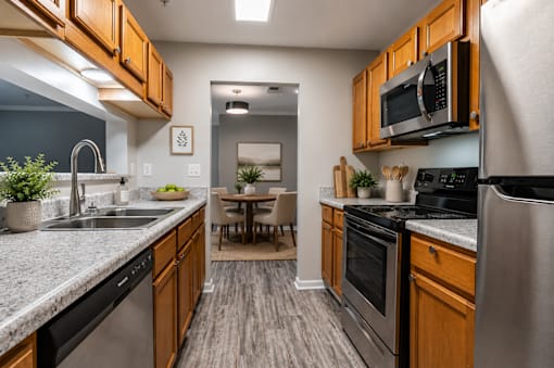 Modern apartment kitchen at Lancaster Place Apartments in Calera, Alabama with stainless-steel appliances, wood cabinetry, generous counter space, and ample storage.