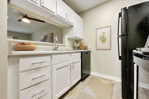 A kitchen with white cabinets and a black fridge.