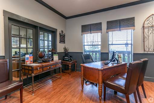 A room with a wooden desk and chair, a couch, and a cabinet with glass doors.