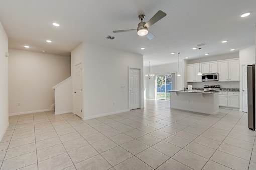 A spacious, empty room with a ceiling fan and tiled flooring.