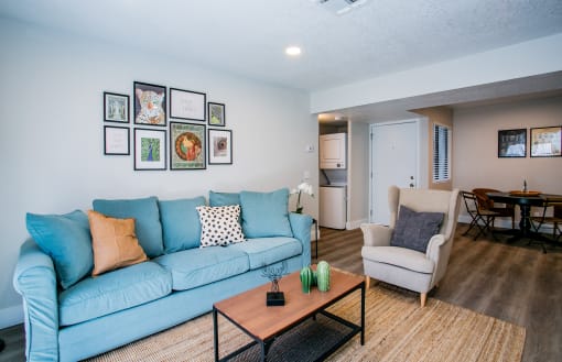 Las Vegas, NV, Apartments Near Big Dogs Brewery - Haven at Lone Mountain - A Living Room With Blue Sofa, Accent Chair, Coffee Table, Wall Art Gallery, and In-Unit Laundry Closet.