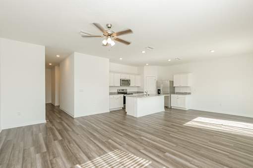 A spacious kitchen and living room with a ceiling fan and lighting.