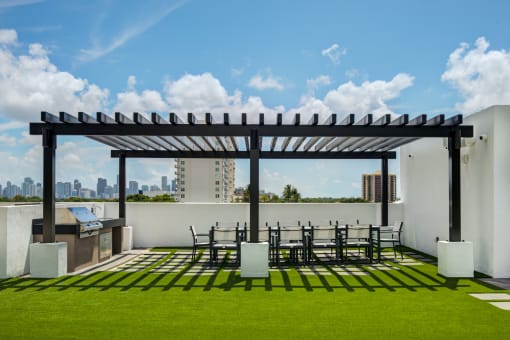 Apartments For Rent In Miami, FL - MB Station - Outdoor Grill Area With Pergola, Expansive Dining Table, Chairs, BBQ Grill, And A Grassy Courtyard