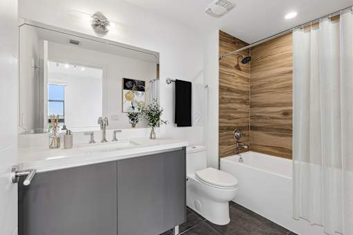 Modern bathroom with quartz vanity, wood-accent shower surround, and contemporary fixtures at MB Station apartments in Coral Way, Miami.