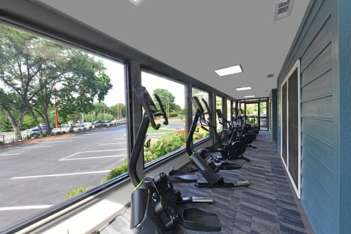 a row of exercise equipment in a gym with large windows