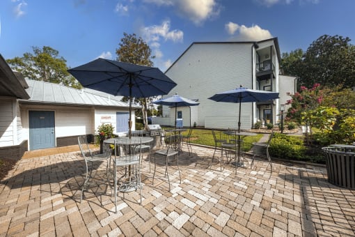 a patio with tables and chairs and umbrellas in front of a house