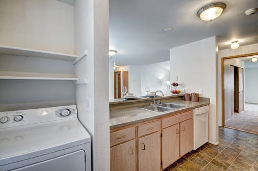 Apartments for Rent in Bothell - North Creek Heights - Kitchen with Beige Countertops, Tan Cabinets, Dual-Basin Sink, Dishwasher, and Adjacent Laundry Equipment