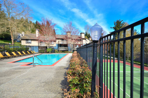 Bothell Apartments for Rent - North Creek Heights - Gated Pool Adjacent to Tennis Court, with Lounge Chairs and Surrounding Lush Greenery