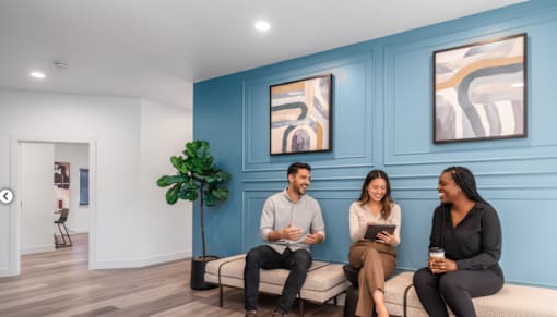 Three people are sitting on a bench in a room with blue walls.