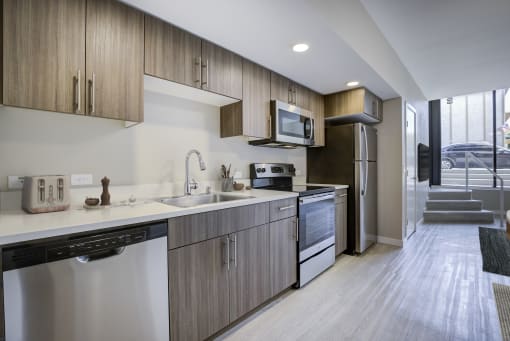 Modern Studio Apartments in Seattle, WA - Origin - Kitchen with Contemporary Wood-Finish Flooring, Stainless Steel Appliances, Stone Countertops, and Wood-Tone Cabinets