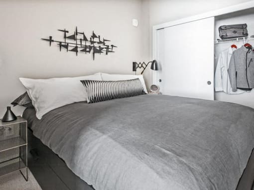 One-Bedroom Modern Apartments in Seattle, WA - Origin - Bedroom with Bed, Nightstand with Lamp, Wall Art, Spacious Closet, and Grey Carpet