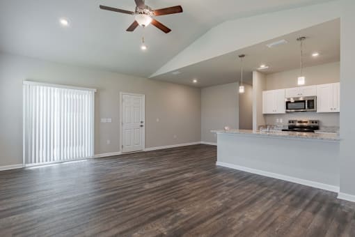 an empty living room with a kitchen and a ceiling fan