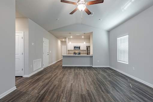an empty living room with a ceiling fan and a kitchen