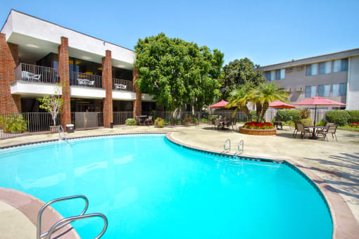 Downey CA Apartments - Park Regency Club - Pool Surrounded By Tables, Chairs, and Umbrellas.