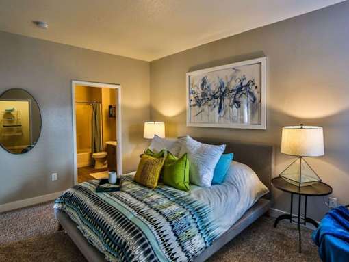 A bedroom with a bed, a side table, and a painting on the wall.