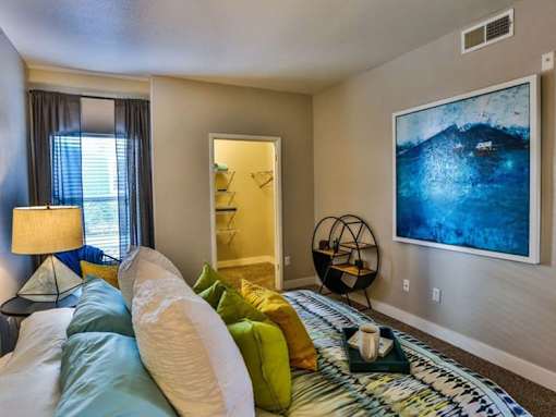 A bedroom with a bed, lamp, and a painting on the wall.