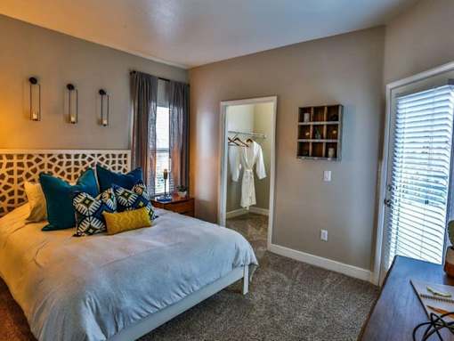 A bedroom with a bed, a mirror, and a window with blinds.