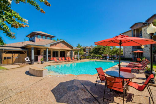 A swimming pool at Lake forest surrounded by beach umbrellas and beach chairs and trees