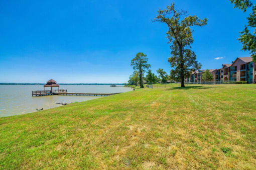 A grassy field with a dock that leads above the water on a bridge to a covering