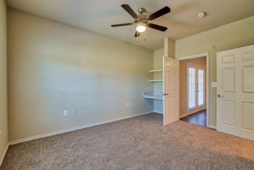 An empty living room with carpet and ceiling fan and shelves and doors