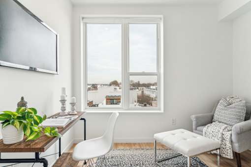 A living room with a white chair, a white ottoman, a white couch, a wooden coffee table, a potted plant, and a framed picture on the wall.