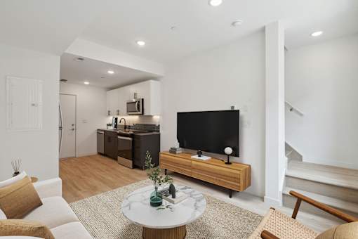 Modern open-plan living space with hardwood flooring, featuring a cozy sitting area with a white round marble-top coffee table, sleek TV stand, and an understairs white door.