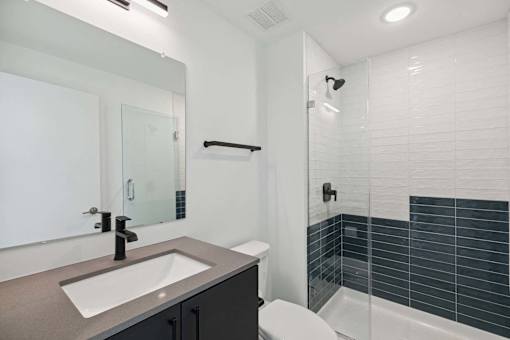 A modern bathroom with a sink, mirror, toilet, and shower.