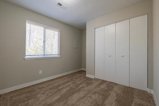 A room with a window and a brown carpet.