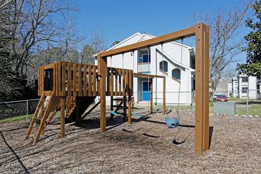 A wooden swing set in front of a white house.