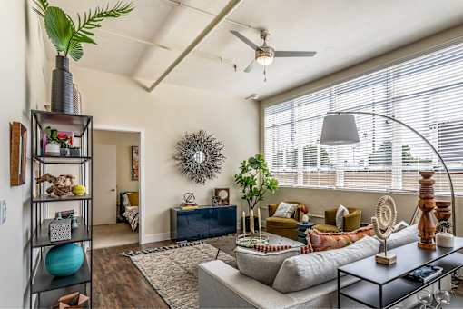 A living room with a large window, a sofa, a coffee table, and a plant on a shelf.