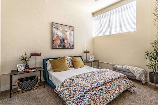 A bedroom with a bed, a nightstand, a plant, and a painting on the wall.