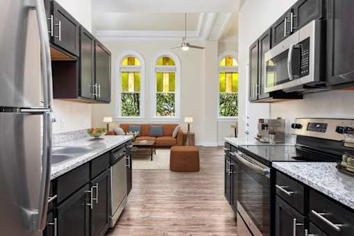 Affordable Apartments Near Concepcion In Park San Antonio, TX - The St. John - A Galley-Style Kitchen With Cabinets, Granite Countertops, And A View Into A Living Area.