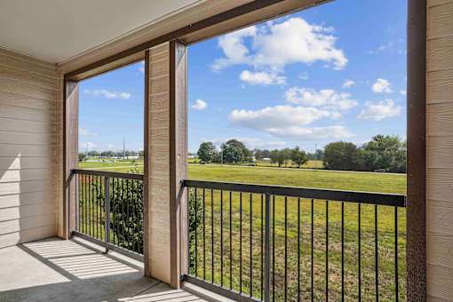 Apartments for Rent in Bentonville, AR 72713– Parc at Bentonville -   A balcony with a view of a grassy field and trees.