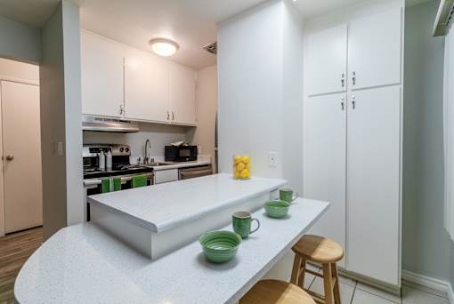 Hayward, CA Apartments Near Hayward BART Station - Paseo Gardens - Kitchen with White Cabinetry, Stainless Steel Appliances, Granite Countertops, Large Pantry Doors, Large Island with Seating and Breakfast Bar Section, and Tile Flooring
